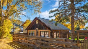 A rustic cabin with a metal roof, wooden walls, and a wooden fence in front. - Walk to Downtown Creede | Pet-Friendly | Mountain Views | Fenced Yard (Creede)