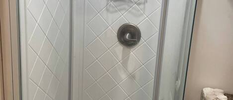 Box de chuveiro com paredes de azulejos em padrão de losangos, um chuveiro e um porta-toalhas de metal.