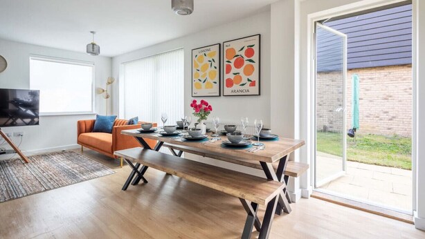 A modern living room with a wooden dining table set for four, a sofa, and a TV.