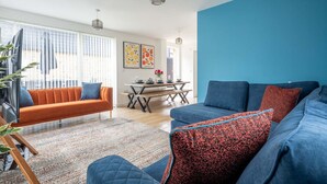 A modern living room with a blue accent wall, a dining area with a wooden table and benches, and a sofa with patterned cushions.