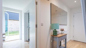 A modern interior with a wooden floor, a grey console table with a green lamp, and a large mirror on the wall.