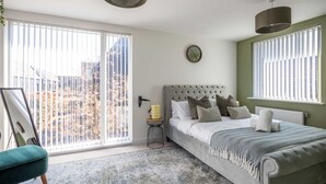 A bedroom with a bed, a bedside table, a clock, and a view of the outdoors through large windows.