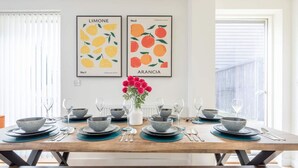 A dining table set with blue and grey plates, bowls, and cutlery, flanked by two framed artworks depicting lemons and oranges.