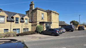 A two-story building with a stone facade, parked cars, and a clear blue sky.