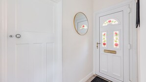 Una puerta blanca con una mirilla y un cerrojo, un pequeño espejo redondo en la pared, y una puerta con un vitral.