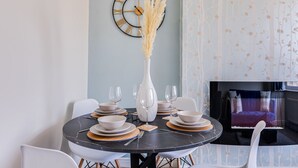 Un comedor con una mesa redonda dispuesta para cuatro personas, un jarrón con plumas de pampa y un reloj de pared.