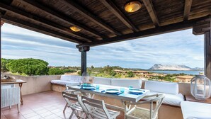 A terrace with a table and chairs, a sofa, and a view of the sea and mountains.