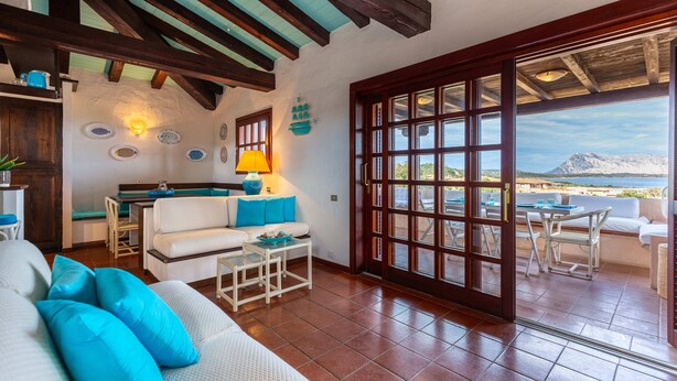 A spacious living area with a white sofa, blue cushions, a small coffee table, and a view of the sea through large glass doors.