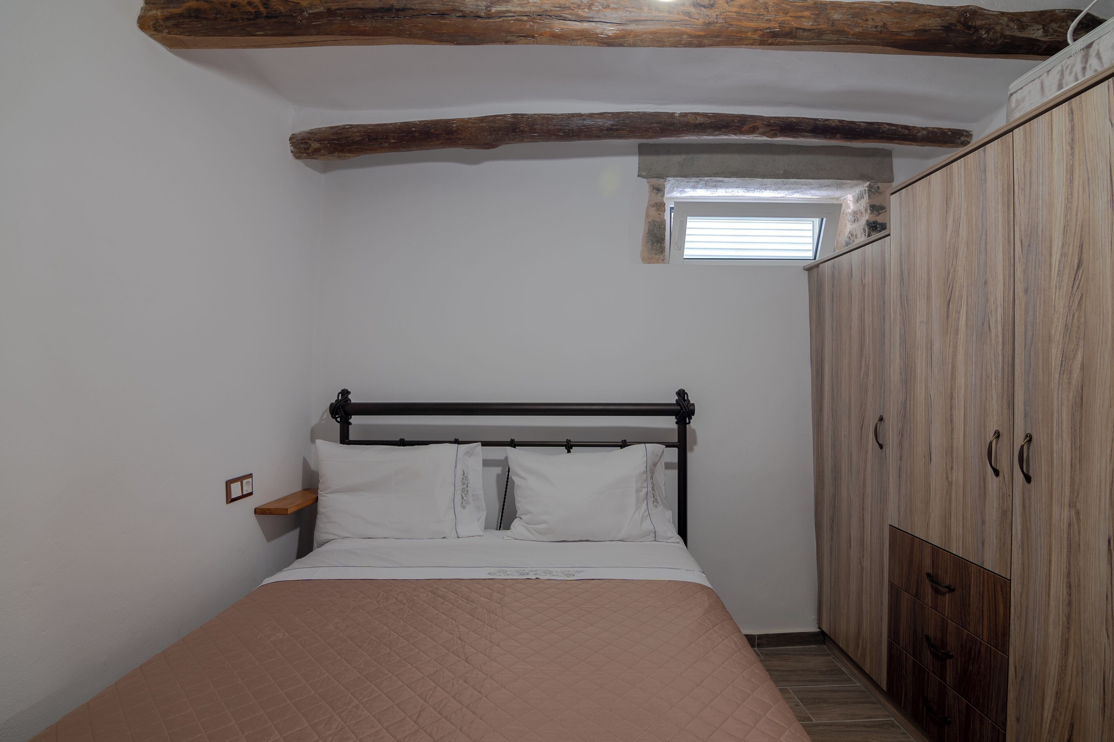 A bedroom with a bed, wooden wardrobe, and a small window.