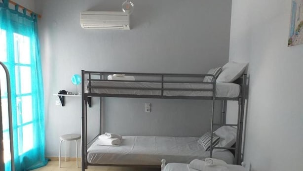 Ein Schlafsaalzimmer mit Etagenbetten, einem kleinen Hocker, einer Wandklimaanlage und einem Fenster mit Vorhängen.