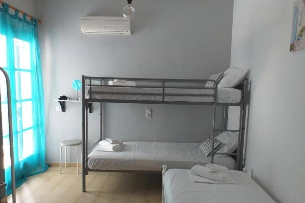 Une chambre de dortoir avec des lits superposés, un petit tabouret, un climatiseur fixé au mur et une fenêtre avec des rideaux.