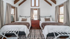 A bedroom with two beds, a wooden dresser, and a window with curtains.