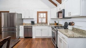 A kitchen with white cabinets, stainless steel appliances, granite countertops, and wooden flooring.