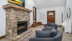 A cozy living room with a stone fireplace, grey sofas, and a wooden door labeled "Blue Ridge."