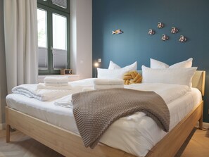 A bedroom with a bed, pillows, a blanket, a window with curtains, a wall clock, and wall art.