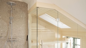 Un baño moderno con cabina de ducha de vidrio, un banco de madera y un tragaluz.