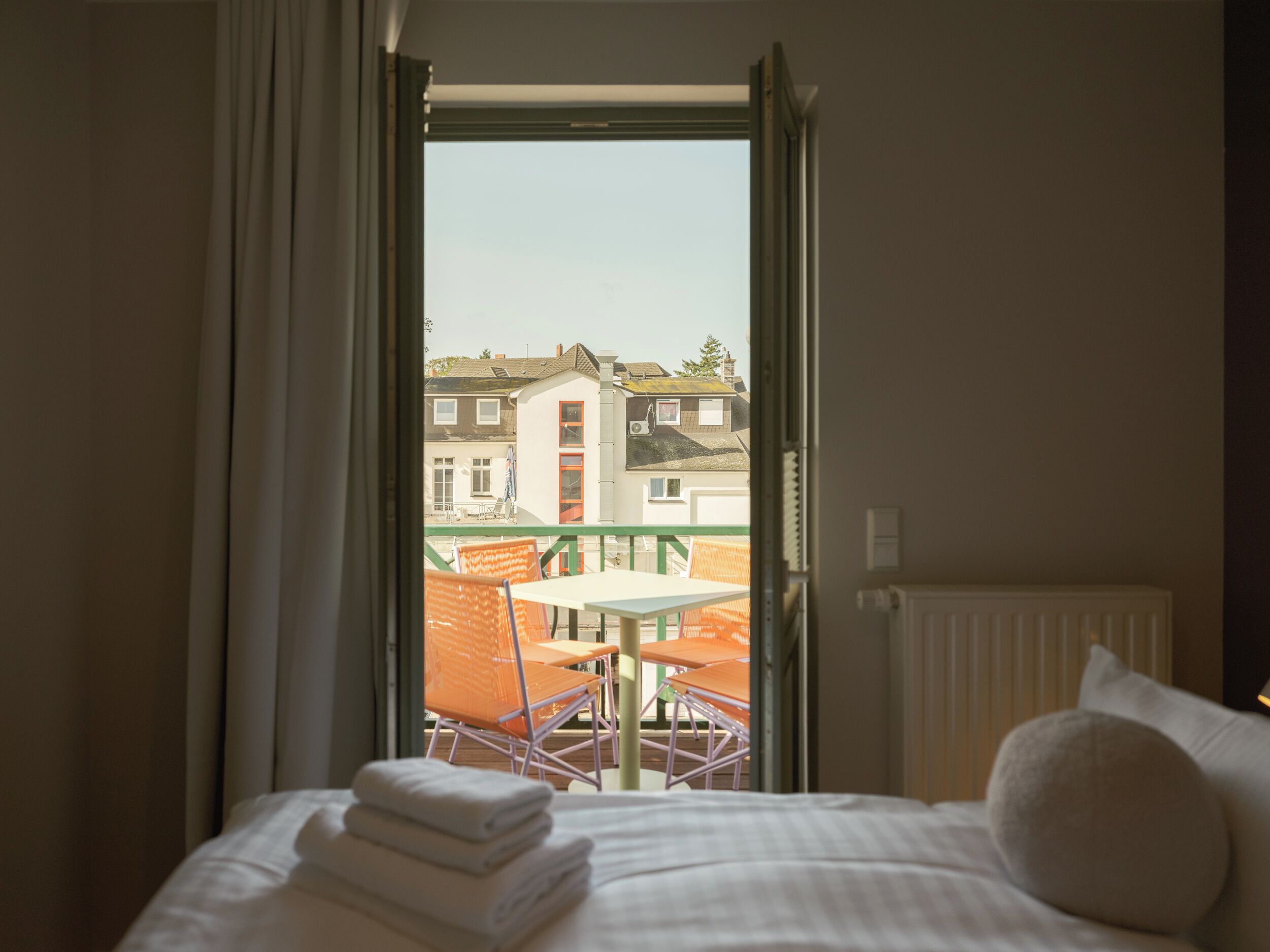 Et hotelværelse med en seng, udsigt til en balkon med bord og stole, samt en bygning i baggrunden.