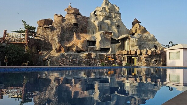 A pool reflecting a rock-like structure with a small building nearby. - Garh Girvar A TJS Unit (Raipur)