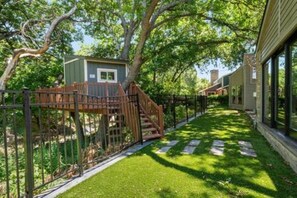 A fenced yard with a wooden deck and a small building, surrounded by trees and a pathway.