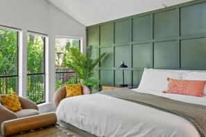 A bedroom with a large bed, a green headboard, and a view of greenery outside.