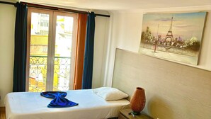 Une chambre d’hôtel avec deux lits, un tableau représentant la Tour Eiffel et une vue sur la ville par la fenêtre.