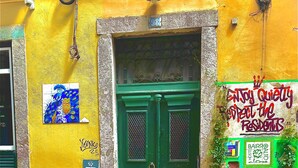 Une porte verte avec un portail en métal, un mur jaune orné d’un numéro, et une affiche colorée sur la droite.