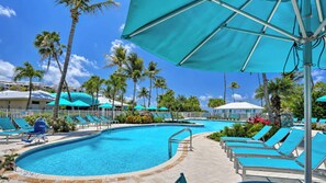 A swimming pool with lounge chairs and umbrellas, surrounded by palm trees and a clear sky.