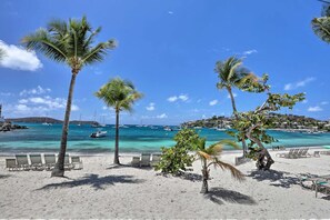 Ein Strand mit Palmen, Liegestühlen und Booten im Wasser.