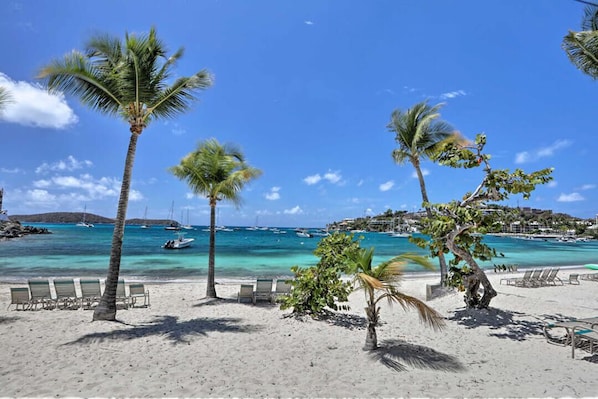A beach with palm trees, lounge chairs, and boats in the water.