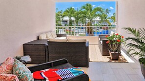 Ein Balkon mit Korbmöbeln, einem Blumentopf und Blick auf Palmen sowie einen Pool.