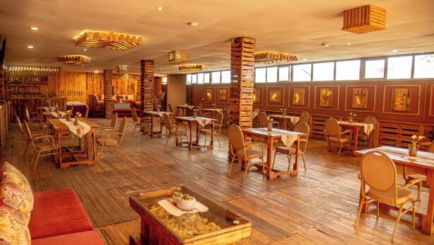A spacious restaurant with wooden flooring, multiple dining tables and chairs, and large windows allowing natural light. - HOTEL GREENWICH (Kigali)