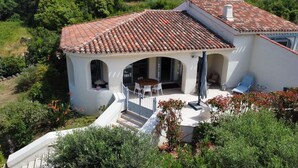 A villa with a tiled roof, a patio with outdoor furniture, and a garden.