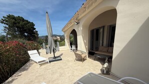 An outdoor patio with white lounge chairs, a table, and an umbrella.