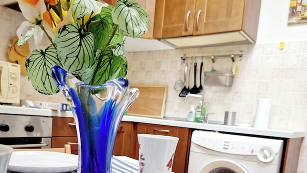 Une cuisine avec des meubles de rangement en bois, un lave-linge et un vase rempli de fleurs posé sur le plan de travail.