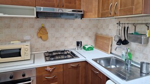 Une cuisine dotée de meubles en bois, d’une cuisinière à gaz, d’un four à micro-ondes et d’un évier en acier inoxydable.