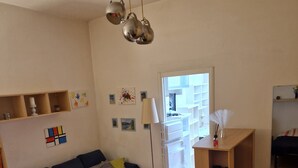 Un salon avec un canapé bleu, une petite table ronde et un meuble blanc. Il y a des étagères au mur et une lampe.