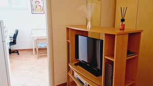 Un espace de vie compact comprenant un téléviseur posé sur un meuble en bois, une petite table et une chaise.