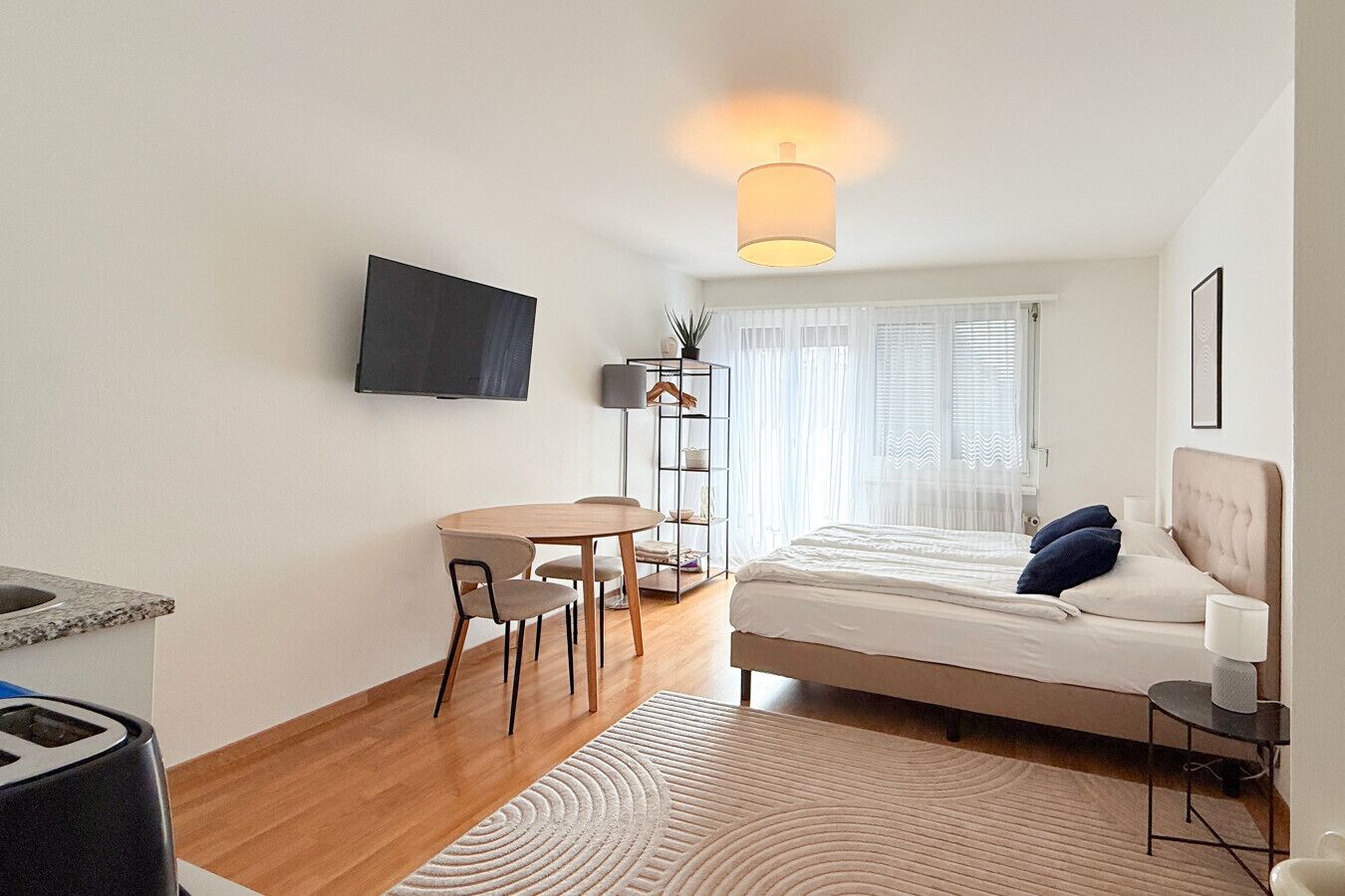 Una habitación de hotel moderna con cama, escritorio, silla, televisor y ventana con cortinas.