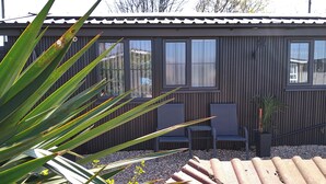 A building with a dark wooden exterior, a tiled roof, and a small garden area with a bench and a potted plant.