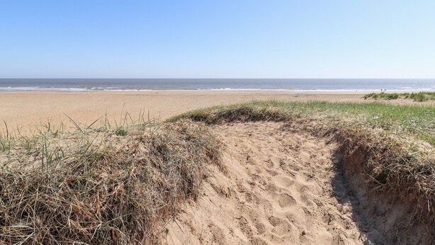 A sandy beach with a clear sky and a grassy dune in the foreground.