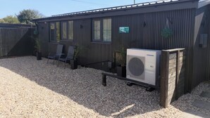 A mobile home with a gravel driveway, a patio with chairs, and a large air conditioning unit.