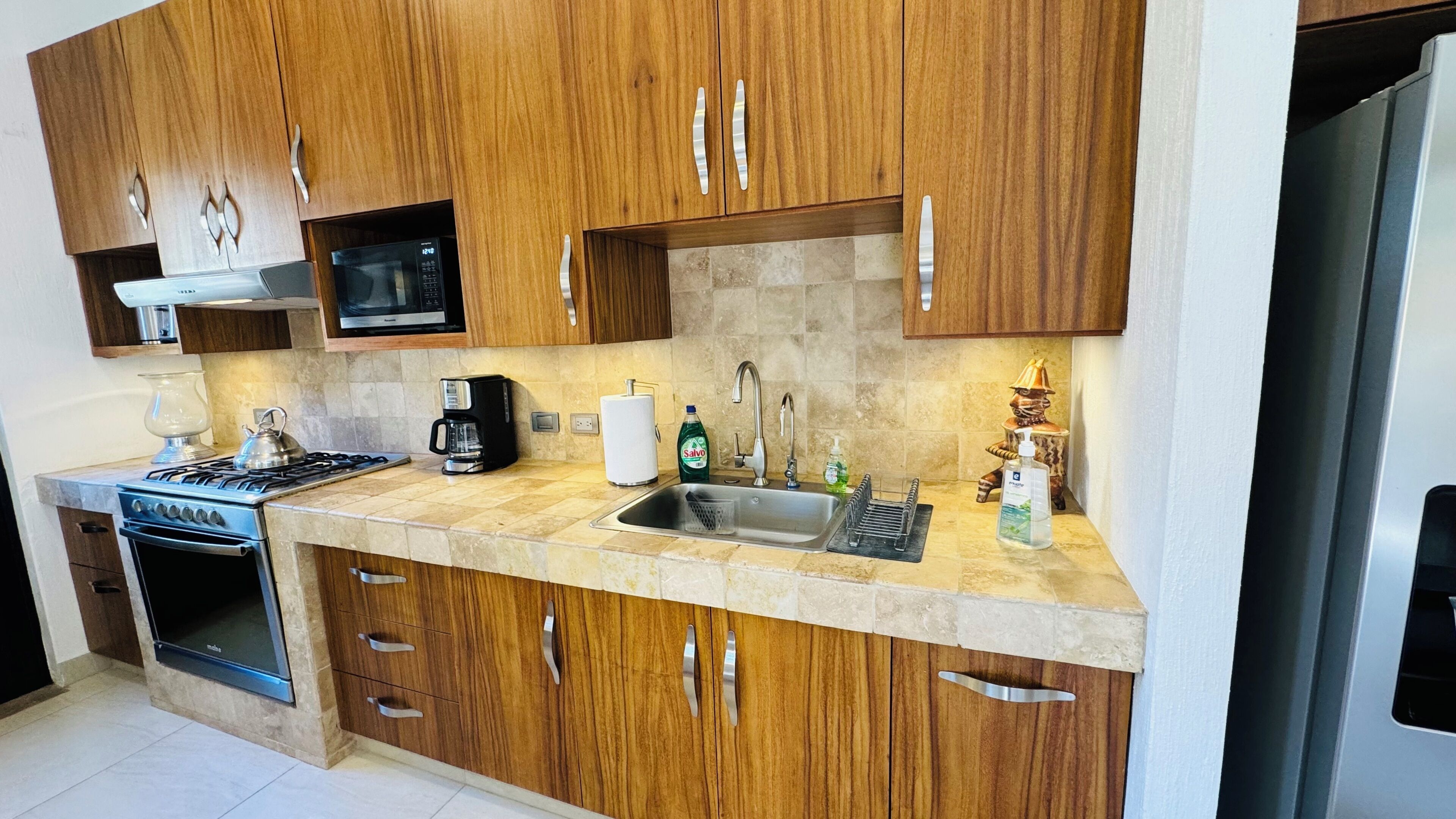 A modern kitchen with wooden cabinets, a stainless steel sink, a microwave, a stove, and a coffee maker.