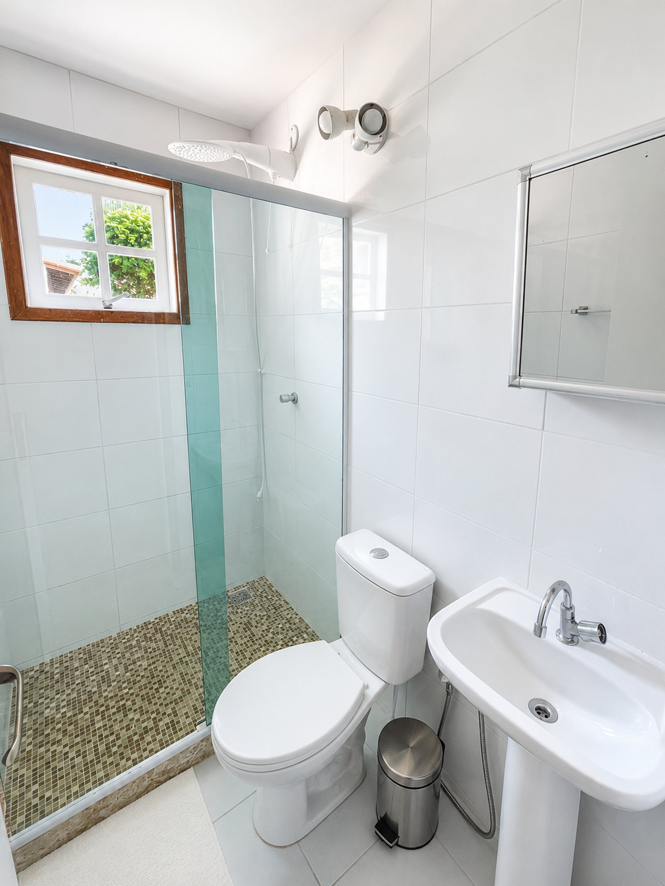 A bathroom with a glass shower enclosure, a toilet, a sink, and a window with a view of greenery.