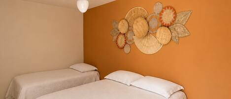 A room with two beds, a ceiling fan, and a wall decorated with woven baskets.