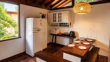 A kitchen with a wooden ceiling, white cabinets, a refrigerator, a microwave, and a dining table set with plates and glasses.