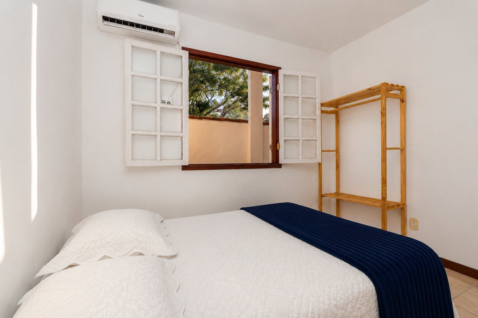 Ein Schlafzimmer mit einem Bett, einem Fenster mit Fensterläden, einer Klimaanlage und einer Holzleiter.