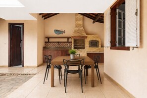 Un coin repas avec une table et des chaises en bois, une plante en pot, un four en briques et une décoration murale représentant des poissons.