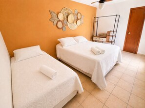 A hotel room with two beds, a wooden door, a ceiling fan, and a wall decoration. - Bz11 Geribá Casa Piscina sauna 6 quartos (Buzios)