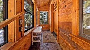 A wooden cabin interior with large windows, a bench, and a door leading outside.