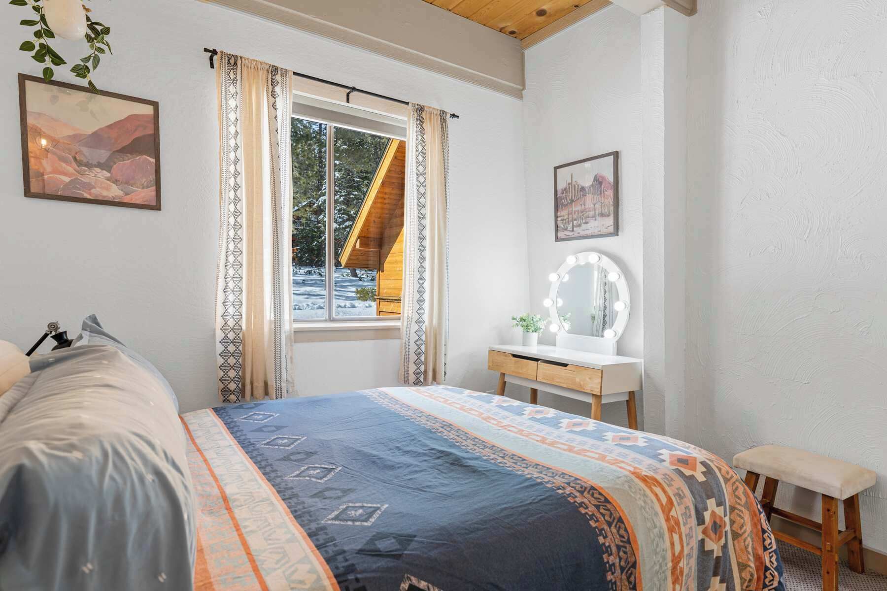 A bedroom with a bed, a vanity with a mirror, and a window with curtains.